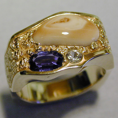 ER-7: A Yogo sapphire from Montana and diamond are a nice addition to this 18 karat gold Elk Ivory band. A nugget texture is used on each side and top of the ring to accentuate the warm color of the gold. For more information please call: (307) 382-3195