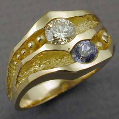 R-9: A diamond and cornflower blue sapphire are center stage on this 18 karat gold band. For more information please call: (307) 382-3195